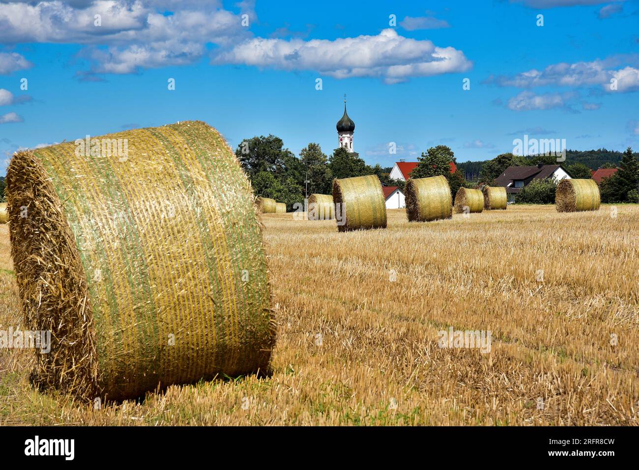 Balle di paglia su un campo di grano raccolto, sullo sfondo la chiesa del villaggio con cupola a cipolla, Baviera, Germania, Europa Foto Stock