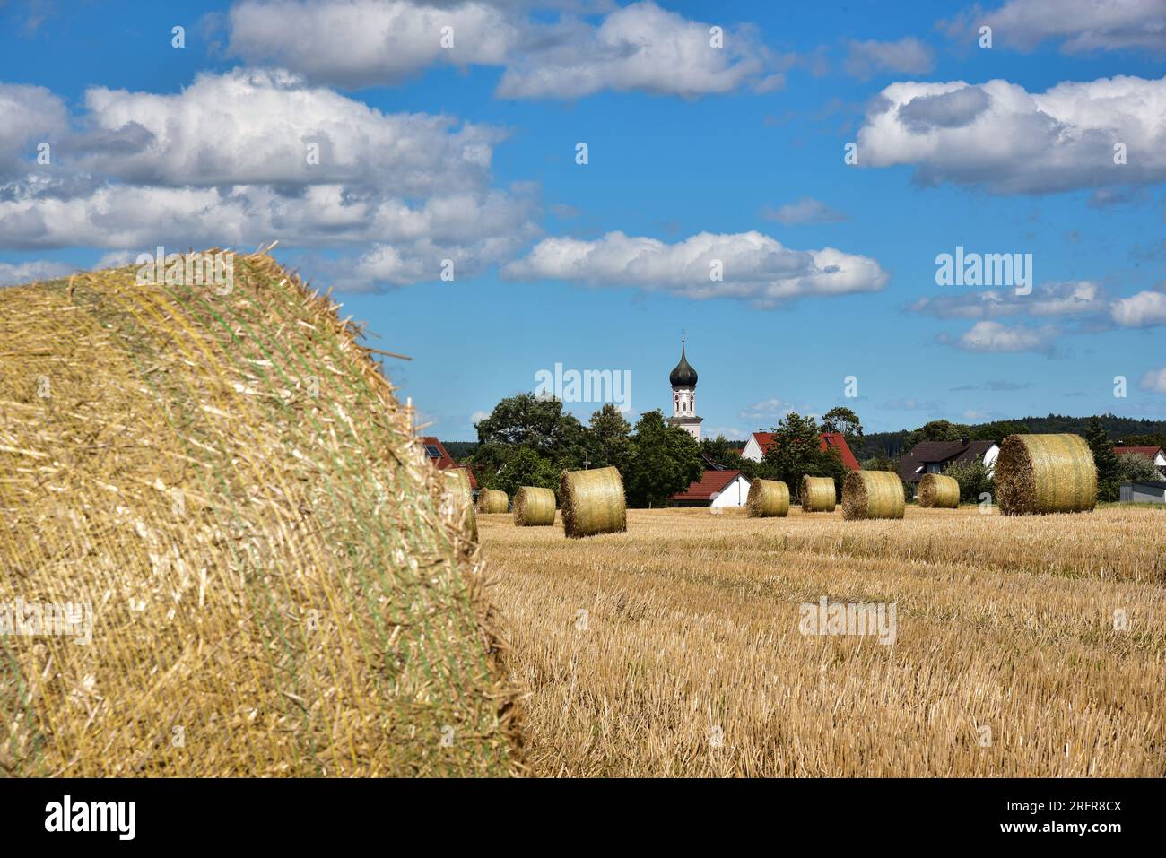 Balle di paglia su un campo di grano raccolto, sullo sfondo la chiesa del villaggio con cupola a cipolla, Baviera, Germania, Europa Foto Stock