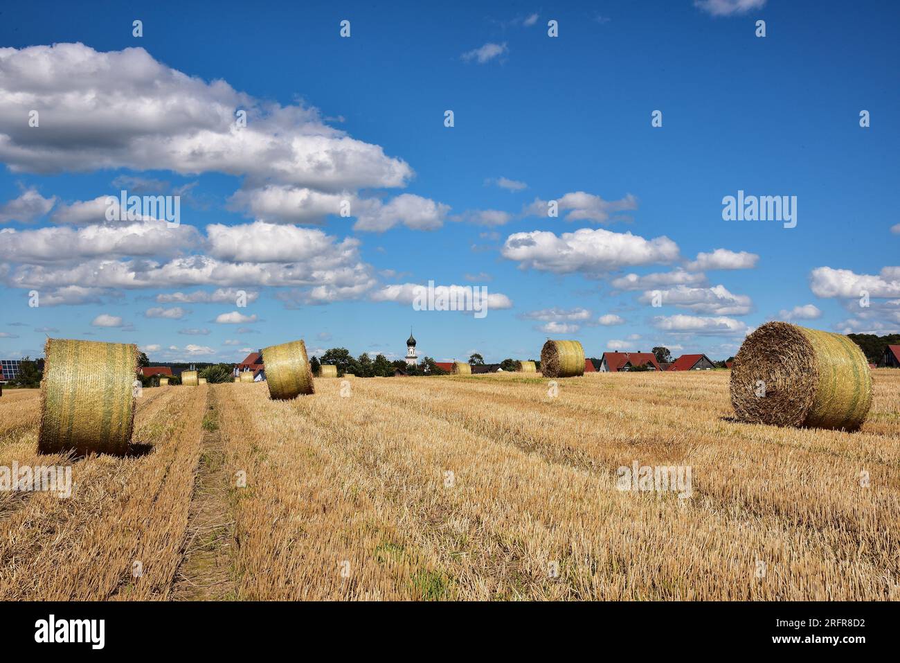 Balle di paglia su un campo di grano raccolto, sullo sfondo la chiesa del villaggio con cupola a cipolla, Baviera, Germania, Europa Foto Stock