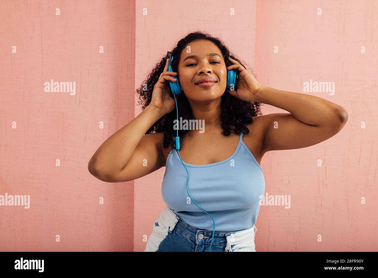 Donna sorridente che ascolta musica con cuffie blu Foto Stock