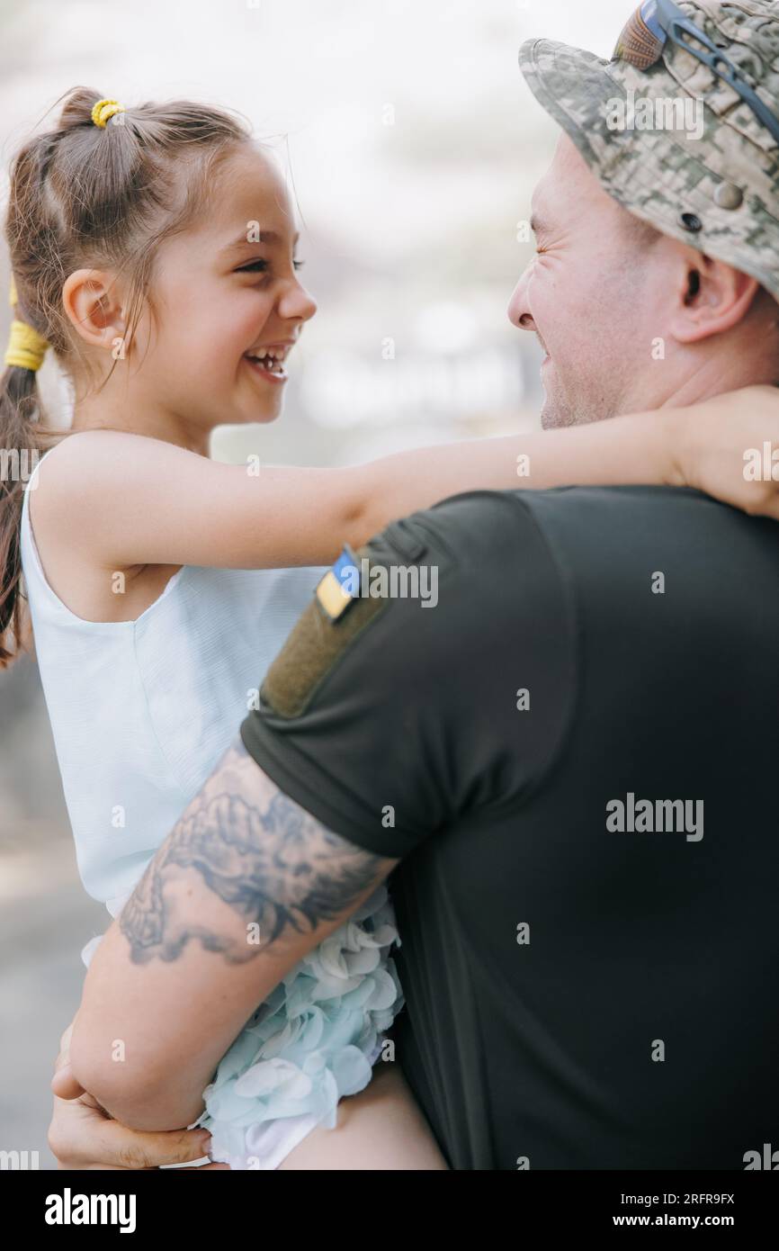 Ritratto del soldato ucraino di ritorno dalla guerra incontrando la sua figlia piccola e Joyful la abbraccia. Guerra in Ucraina. Invasione militare russa in Foto Stock