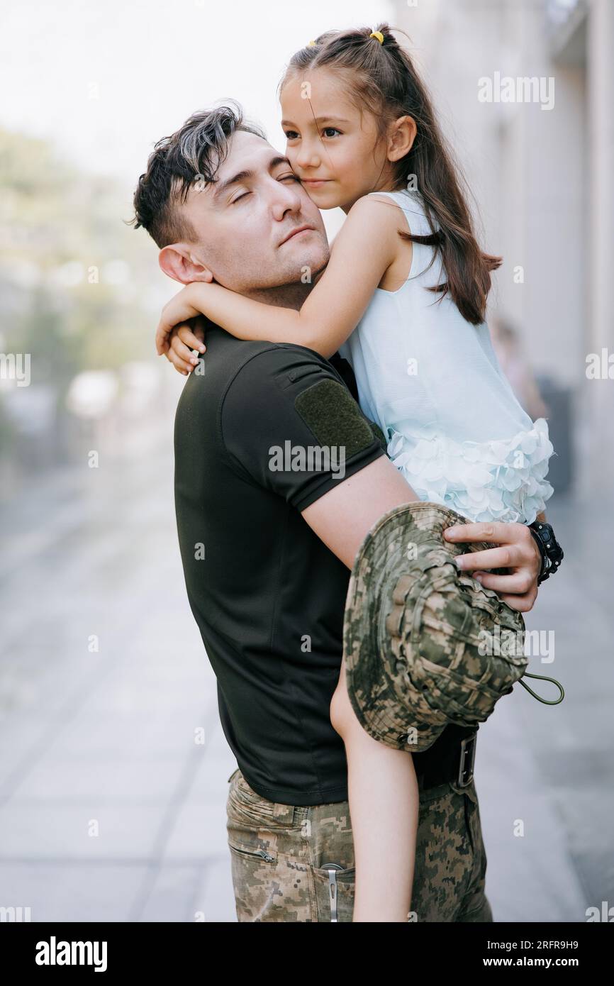 Felice soldato ucraino di ritorno dalla guerra incontra la sua piccola figlia e la abbraccia. Guerra in Ucraina. Invasione militare russa in Ucraina. Guerra a Foto Stock