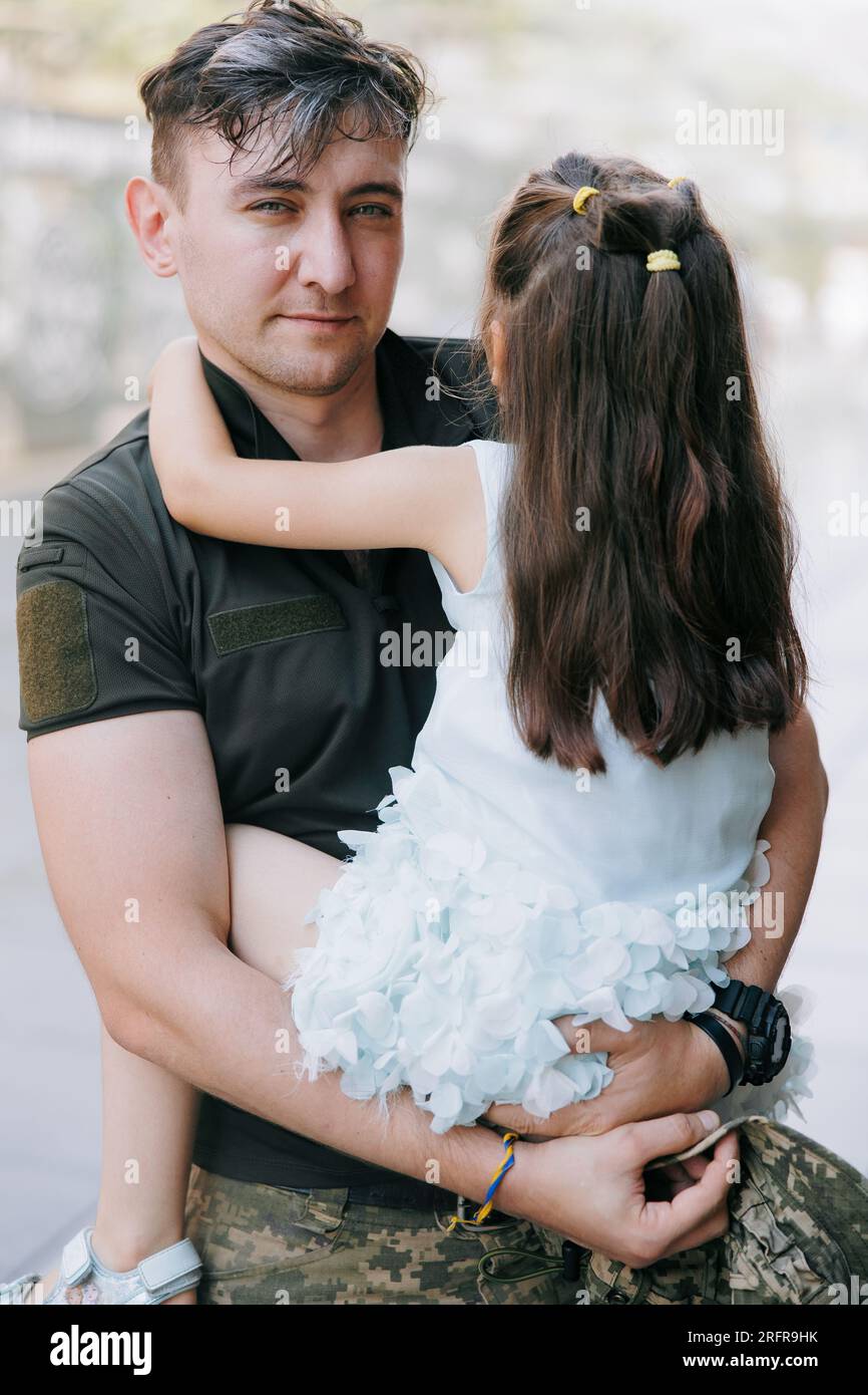 Ritratto di un felice soldato ucraino di ritorno dalla guerra, che incontra la sua piccola figlia e la abbraccia. Guerra in Ucraina. Invasione militare russa i Foto Stock