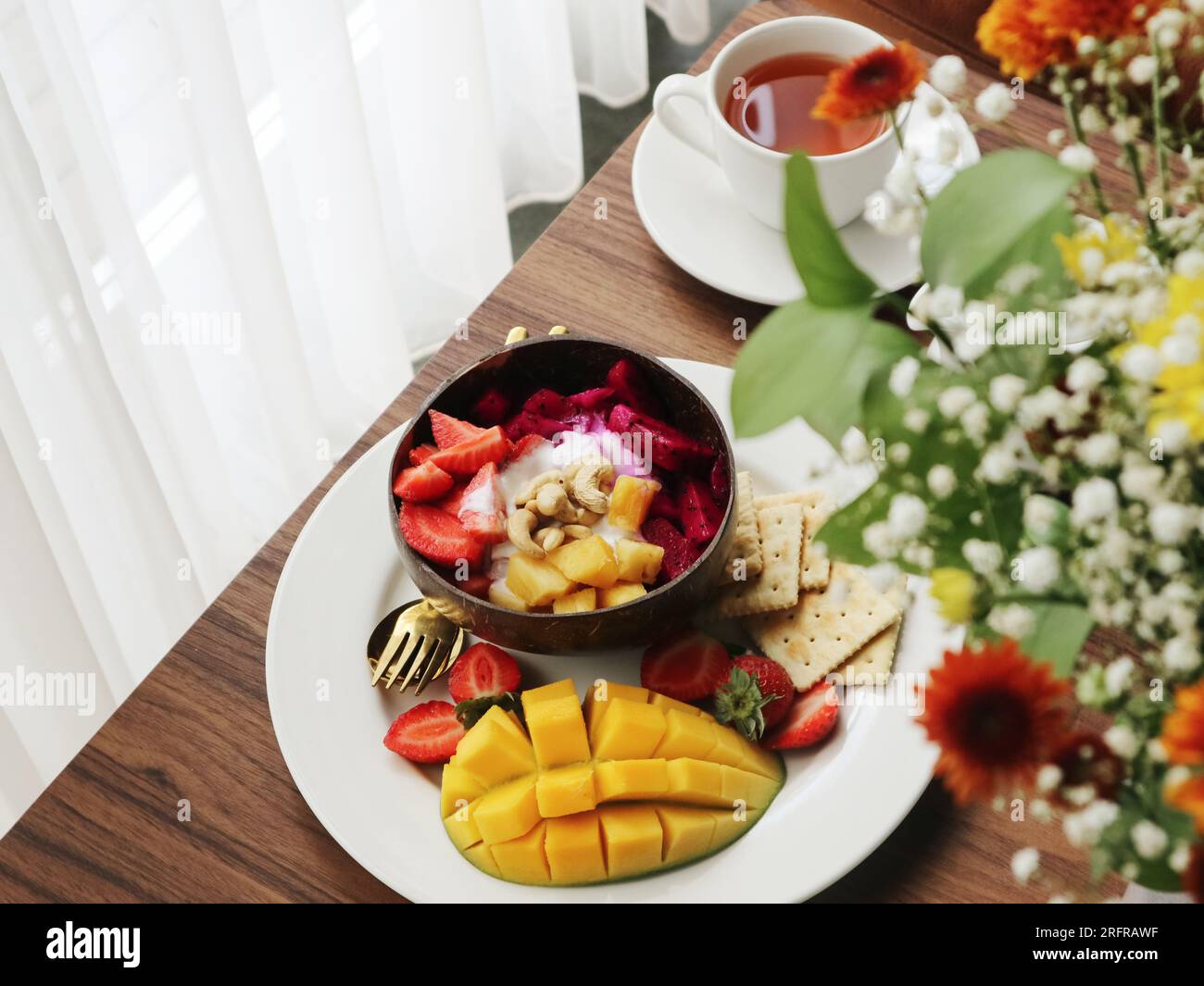 Recipiente per frullato con mango, fragole, frutta di drago e anacardi in un primo piano della ciotola di cocco Foto Stock