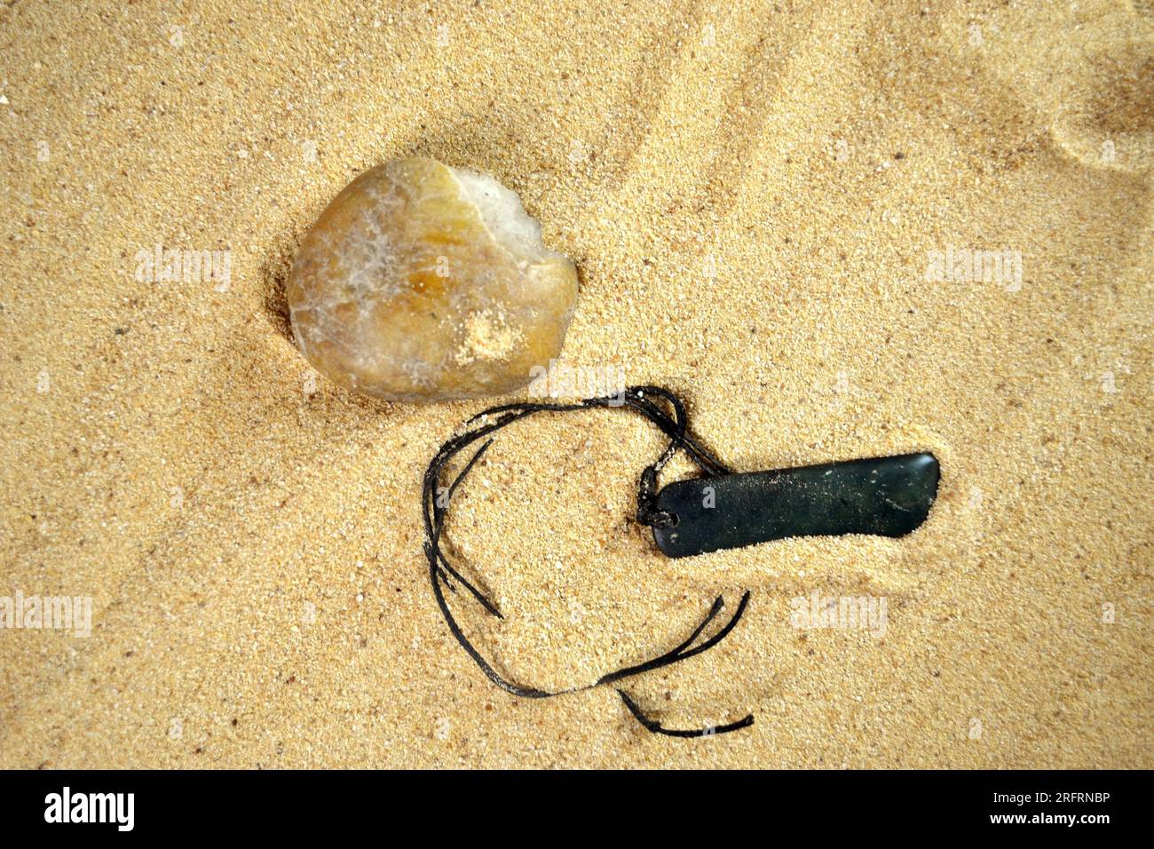Una collana di pietra verde scuro perduta con una pietra naturale sulla spiaggia Foto Stock