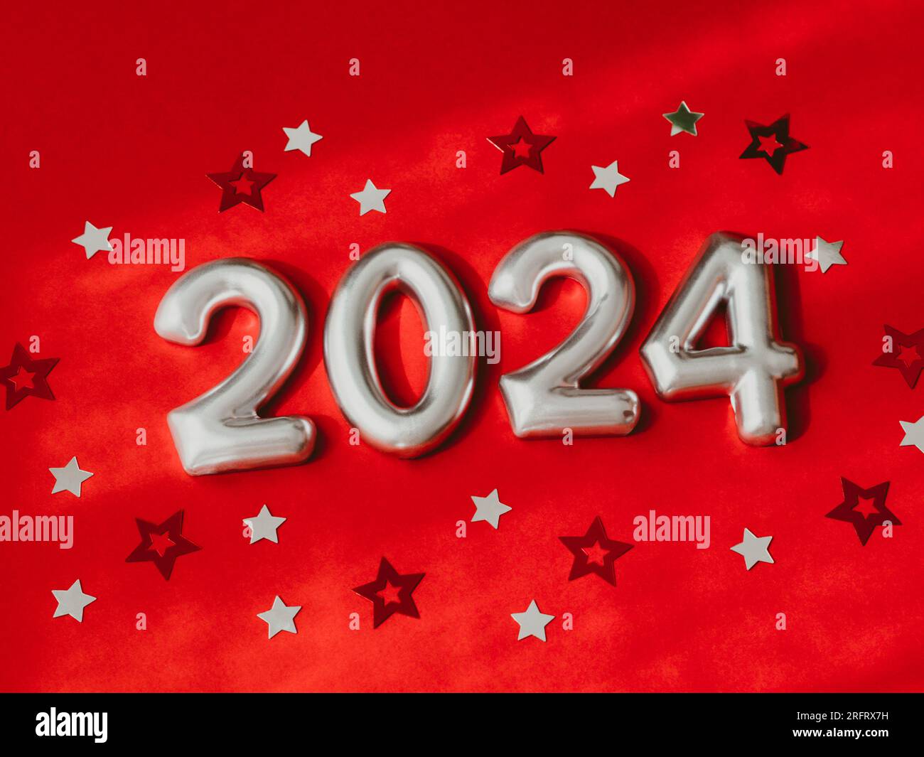 Biglietto d'auguri - buon anno con i numeri 2024 e glitter a forma di stella su sfondo rosso con ombra. Luminoso concetto di vacanza. Vista dall'alto. Copia spazio Foto Stock