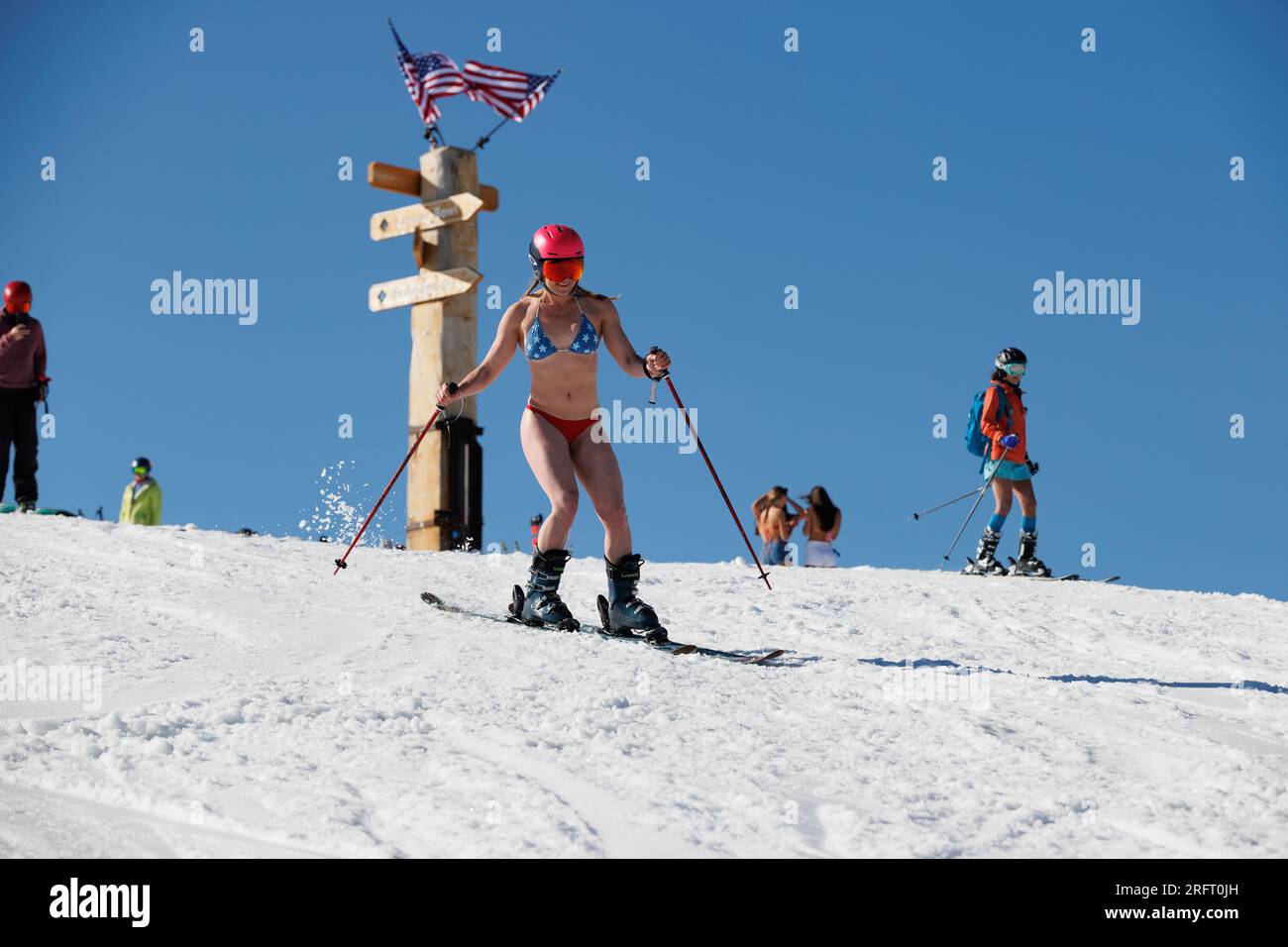 Mammoth Lakes, CA. 4 luglio 2023. Una donna in forma in bikini e sci con casco davanti alle bandiere americane al Mammoth Mountain Ski Resort in una chiara giornata estiva. Foto Stock
