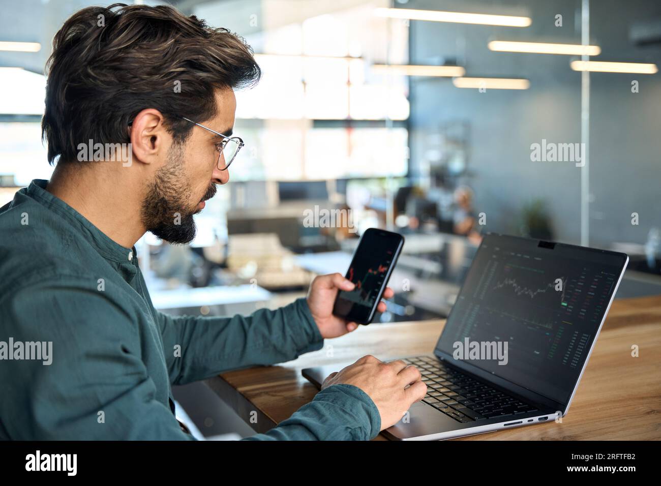 Investitore azionario che tiene telefono utilizzando un computer portatile che analizza i dati del mercato commerciale. Foto Stock