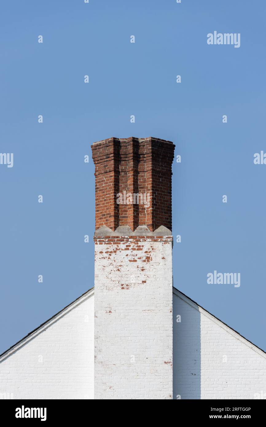 un camino unico di mattoni rossi con angoli geometrici sulla sommità di un tetto di mattoni bianchi contro un cielo blu cristallino, spazio copia Foto Stock