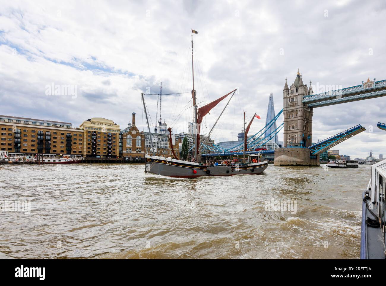La chiatta a vela del Tamigi passerà sotto il Tower Bridge aperto presso Butlers Wharf, Bermondsey, nella Docklands Pool di Londra Foto Stock