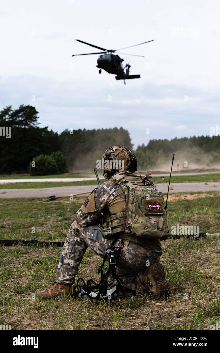 Un controllore della zona di carico con le forze Armate nazionali lettoni osserva un UH-60 Falco Nero mentre si avvicina alla zona di atterraggio durante il concorso NATO Best Sniper Competition 2023 tenutosi a Camp Adazi, Lettonia, 1 agosto. Il concorso, sostenuto da equipaggi di elicotteri con la Task Force Knighthawk, 3rd Combat Aviation Brigade, a sostegno della 4th Infantry Division, consisteva in tre squadre in rappresentanza di 12 alleati della NATO: Bulgaria, Canada, Croazia, Estonia, Finlandia, Italia, Lettonia, Lituania, Norvegia, Spagna, Il Regno Unito e gli Stati Uniti. Il 4° Inf. La missione del Div. In Europa è impegnarsi in multinazionali Foto Stock