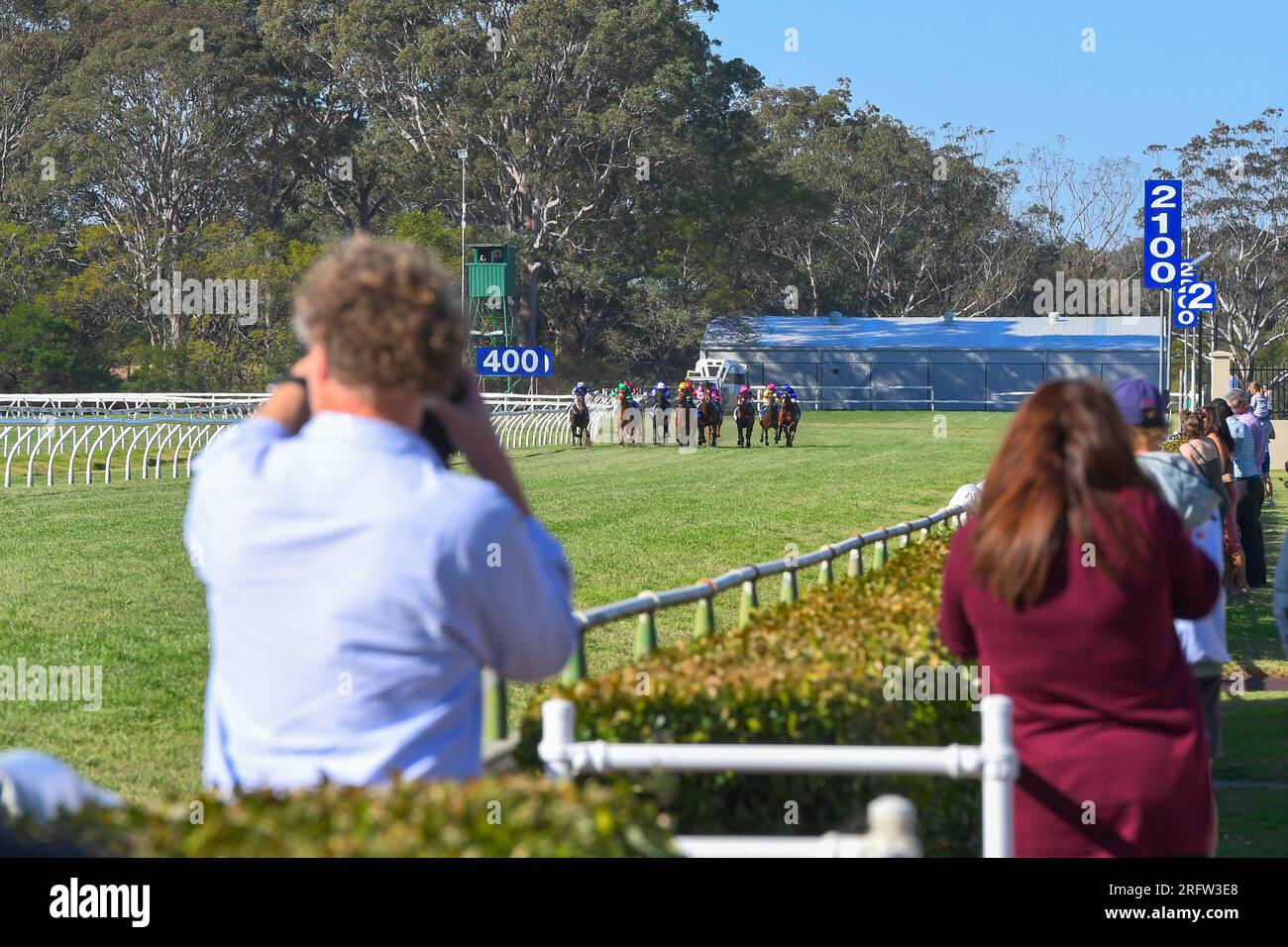 Gli spettatori all'ippodromo guardano la fine di una corsa di cavalli e scattano foto Foto Stock
