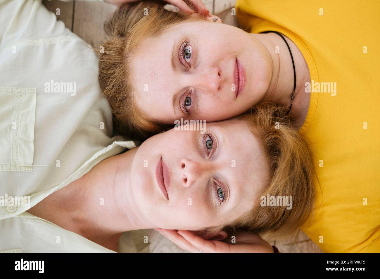Due sorelle dai capelli rossi si stagliano dalla guancia e guardano la fotocamera. Donne simili con pelle chiara e lentiggini. Foto Stock