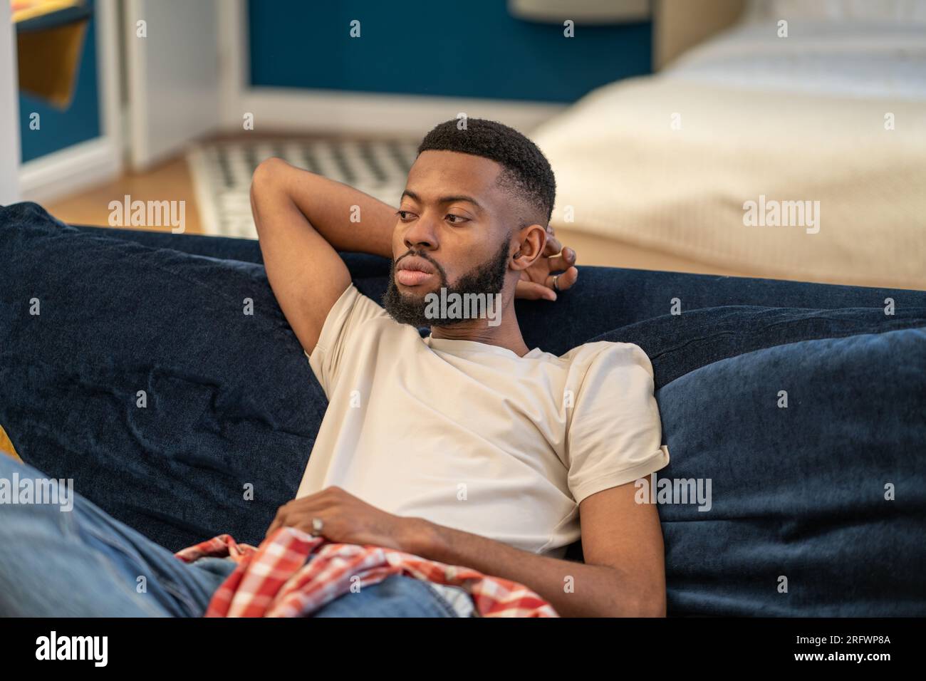 Il ragazzo afro-americano sognante e premuroso siede su divani appoggiati nel monolocale. Foto Stock