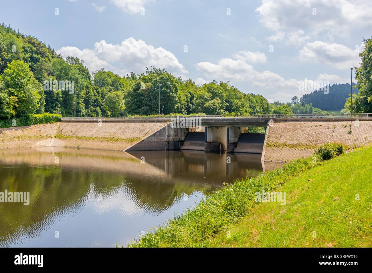 Diga di Staumauer Bitburger sul fiume Prum, riflesso sulla superficie dell'acqua, ponte veicolare, alberi frondosi verdi sullo sfondo, serbatoio di Stausee Bitburg su un Foto Stock