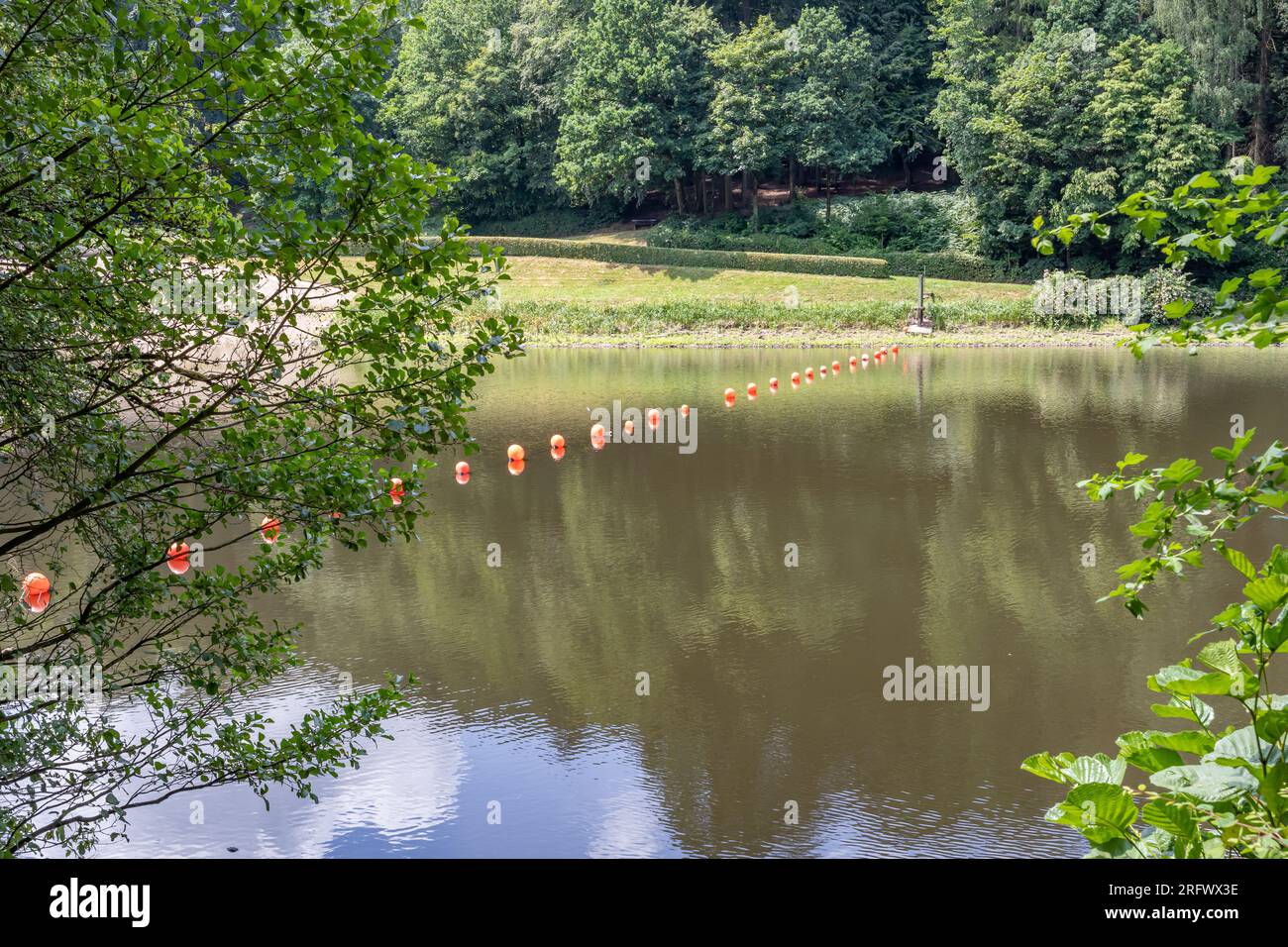 Fiume Prum nel bacino idrico di Stausee Bitburg con boe arancioni e riflessi sulla superficie dell'acqua, alberi verdi sullo sfondo, soleggiato giorno primaverile Foto Stock