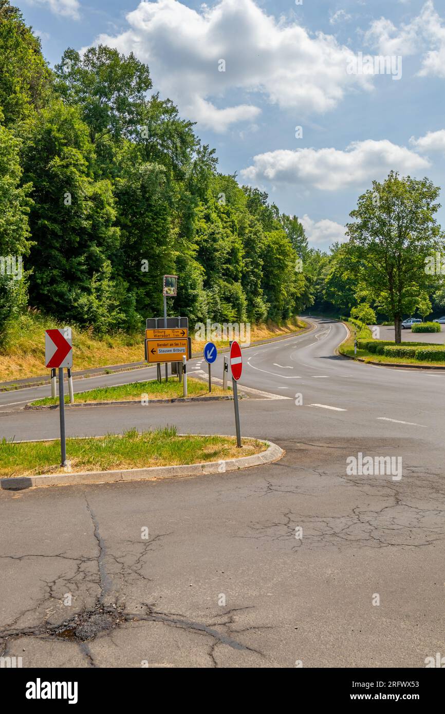 Vari segnali stradali su una strada di campagna vuota: Nessun ingresso, attenzione, indicazioni stradali e indicazioni per le città, parcheggio pubblico e alberi frondosi in ba Foto Stock