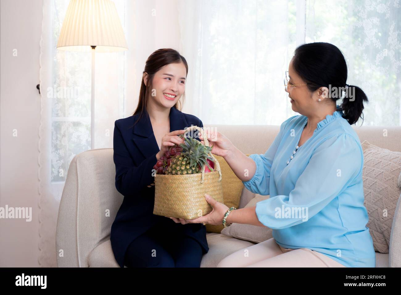 Assicurazione agente giovane donna asiatica visita il cliente anziano mentre dà un cesto di frutta in soggiorno a casa, donna d'affari o consulente che parla e. Foto Stock