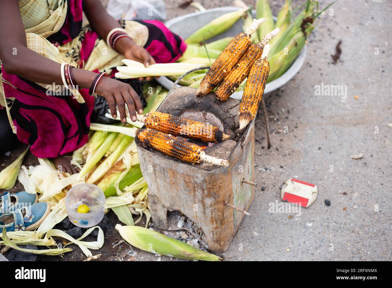 Una povera donna indiana non identificabile che vende mais arrosto in un negozio di strada o di strada Foto Stock