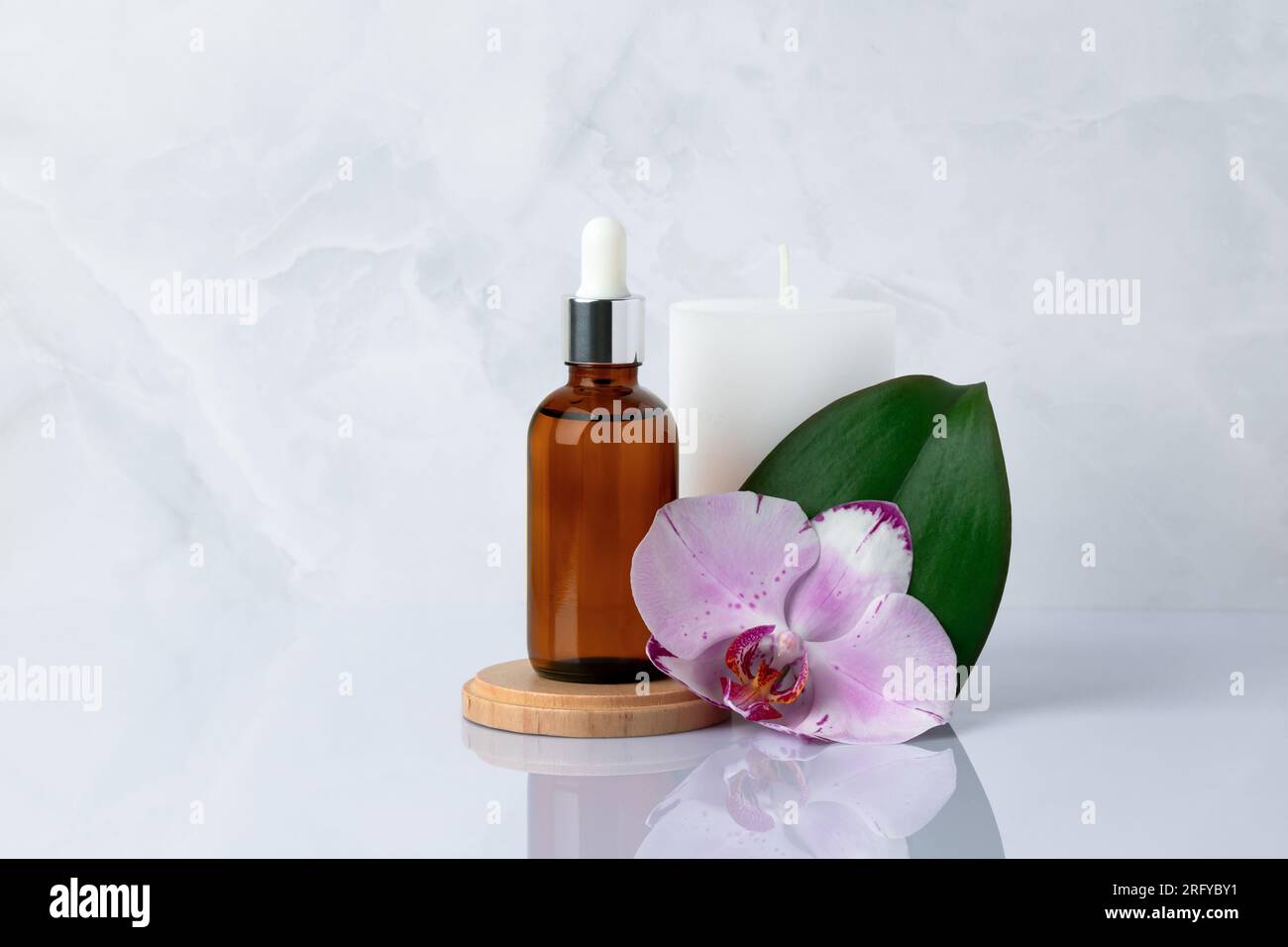 Primo piano del siero del viso. Una bottiglia di vetro con contagocce. Olio aromatico per massaggi su fondo di marmo grigio e fiore di orchidea vicino. Cosmetici naturali biologici spa Foto Stock