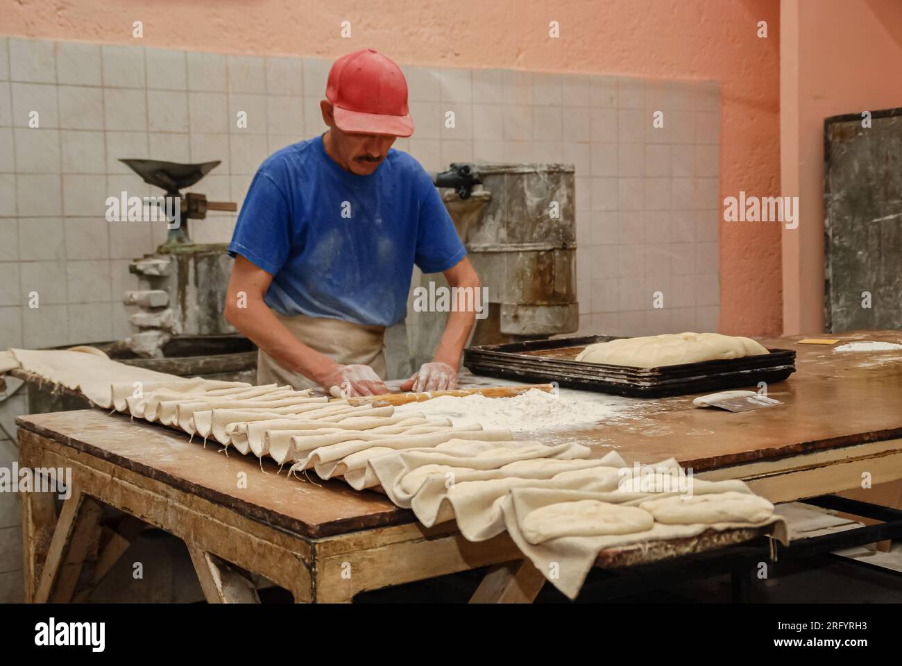 In una panetteria tradizionale messicana riccamente dettagliata, il panettiere corposo realizza empanadas con precisione. Il suo corpo e' completamente visibile, con un cappello che ombreggiava Foto Stock