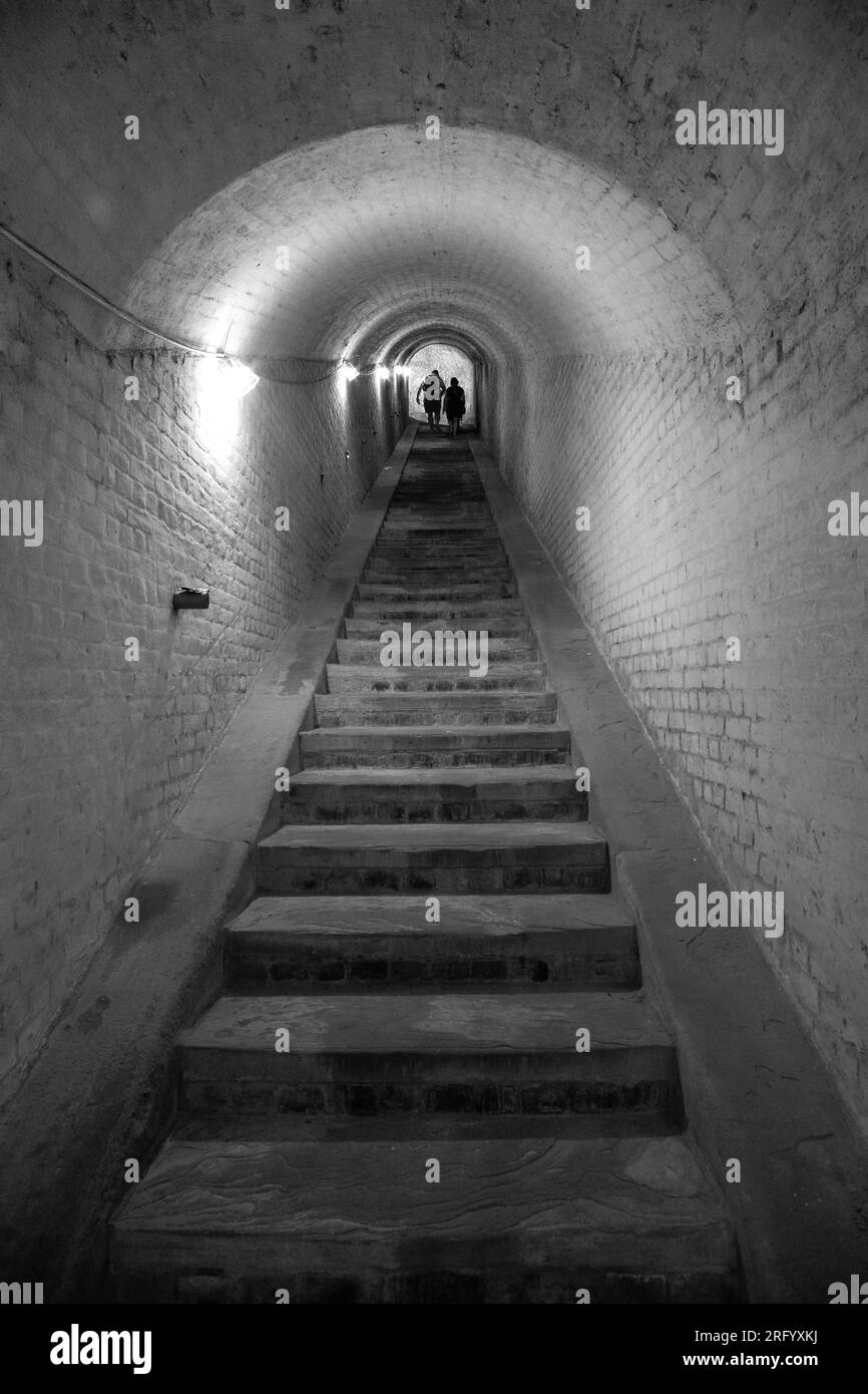 Foto monocromatica di scale in pietra all'interno di un tunnel al forte Drop Redoubt di dover, Inghilterra, con un gruppo di persone in cima. Foto Stock