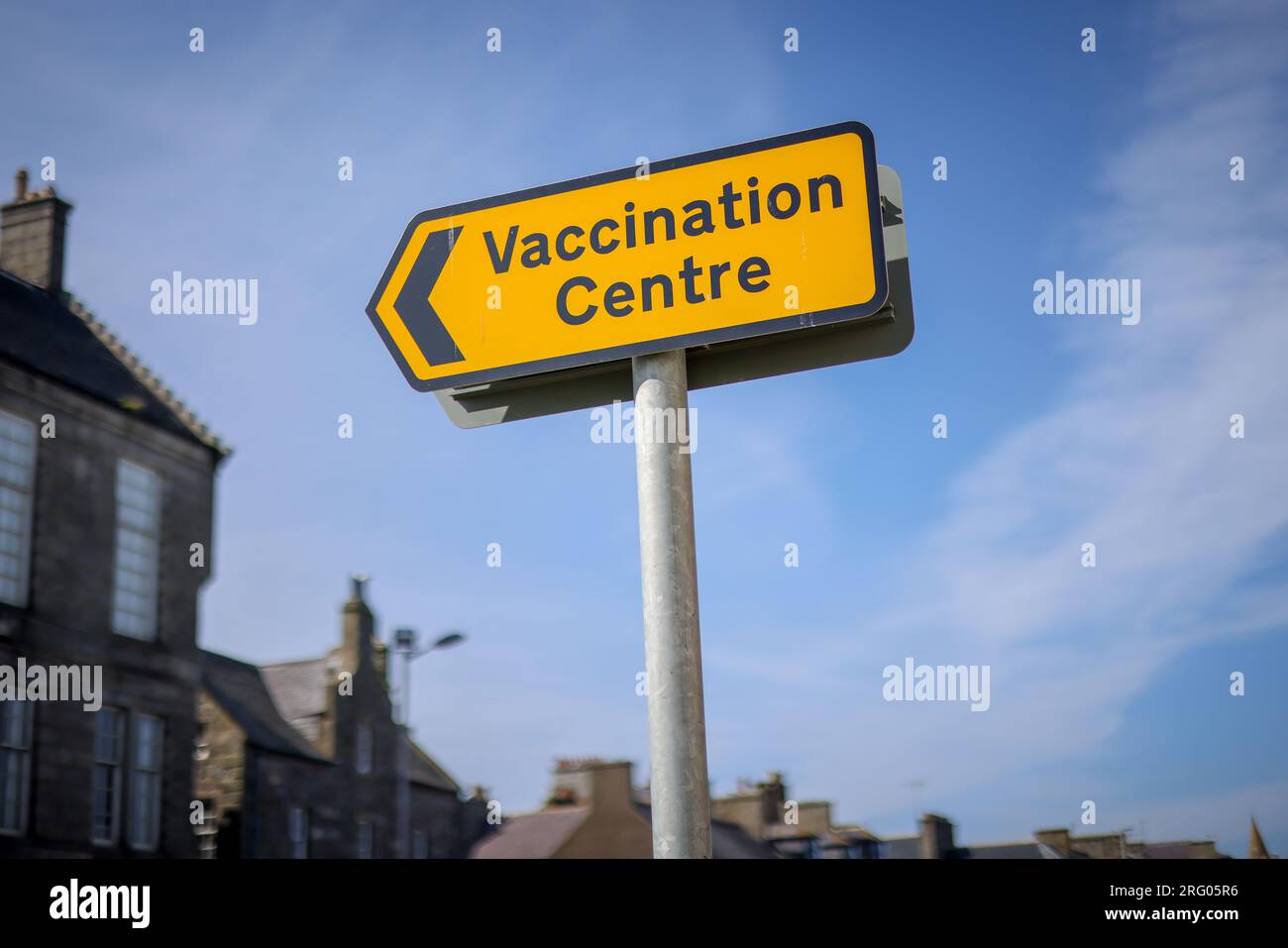Segno giallo del "centro di vaccinazione" COVID-19 contro il cielo blu. Preso a Fraserburgh, nel nord-est della Scozia. Foto Stock