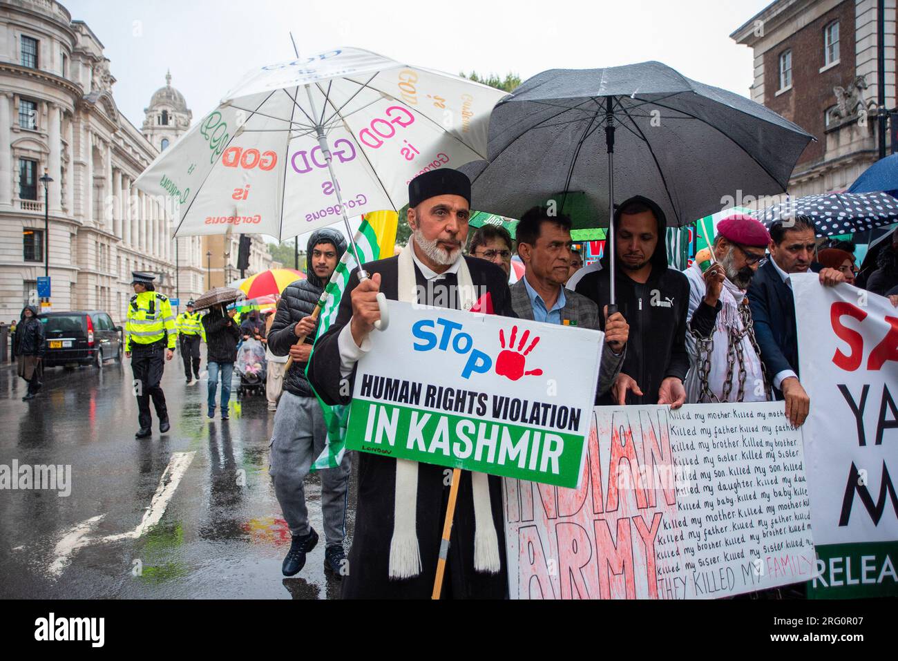 Imam tiene un cartello e un ombrello mentre marcia sul fronte con gli altri manifestanti durante la manifestazione. La diaspora del Kashmir a Londra marciò verso l'alta Commissione indiana chiedendo il rilascio di tutti i prigionieri politici, tra cui Yasin Malik. Yasin Malik è un leader separatista ed ex militante. Vuole la separazione del Kashmir sia dall'India che dal Pakistan. È il presidente del fronte di liberazione del Kashmir Jammu. Fu giudicato colpevole di cospirazione criminale e di guerra contro lo Stato e fu condannato all'ergastolo in India. Foto Stock