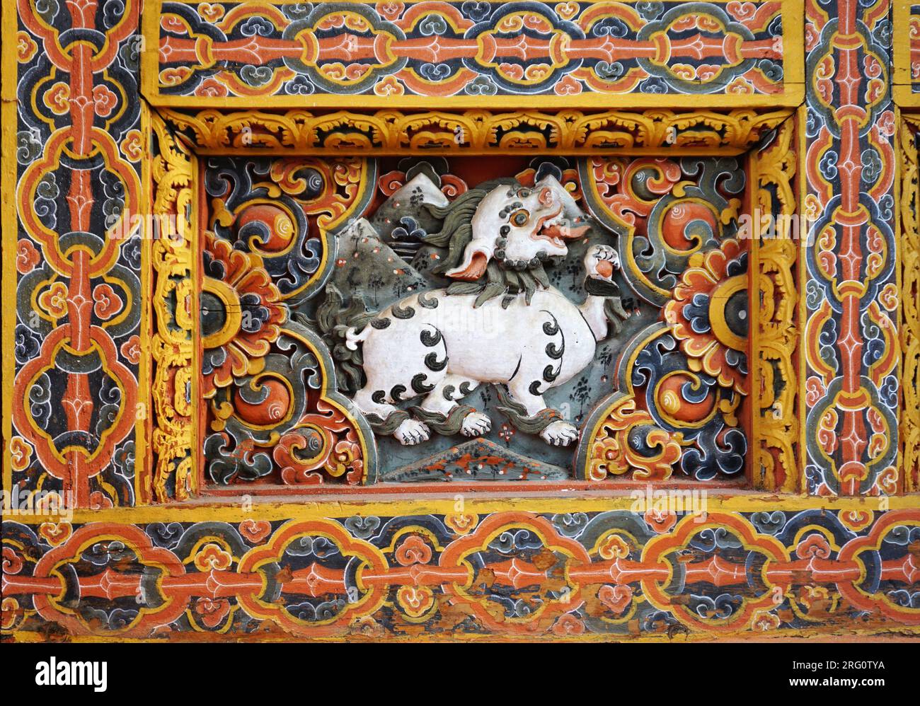 Primo piano di un rilievo in legno dipinto intagliato con un mitico leone bianco di neve circondato da intricati ornamenti dipinti a Punakha Dzong, Bhutan Foto Stock