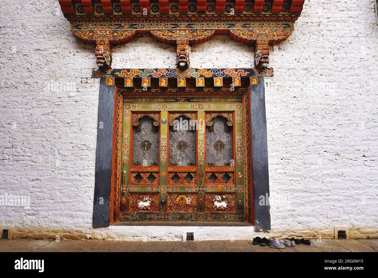 Trittico di pannelli di legno intagliati e dipinti con pesante struttura in legno e tre draghi sopra, incastonato in un muro di pietra bianca a Punakha Dzong, Regno del Bhutan Foto Stock