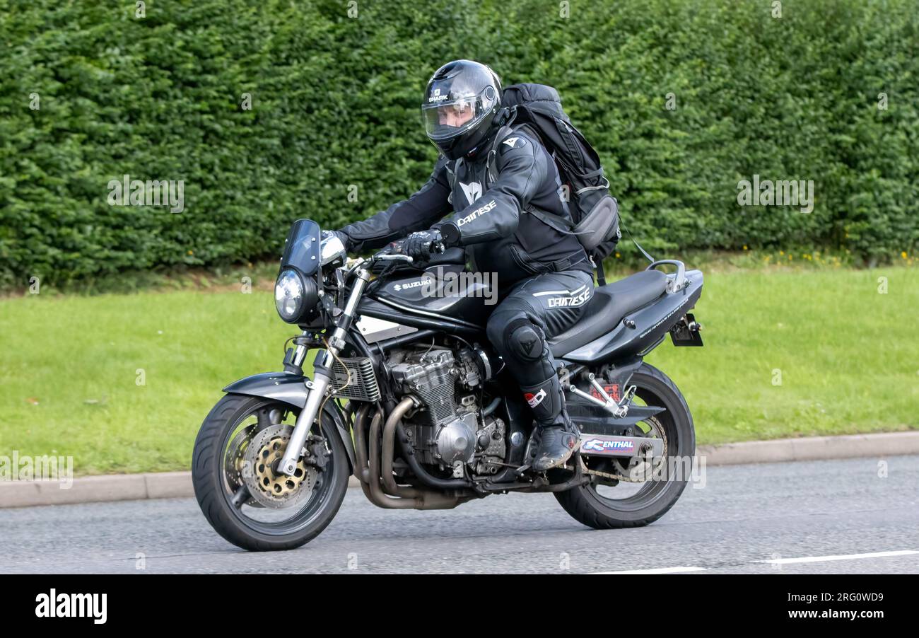 Whittlebury, Northants., UK - 6 agosto 2023. Uomo che indossa pelli da moto nere in sella a una Suzuki nera attraverso un villaggio inglese. Foto Stock