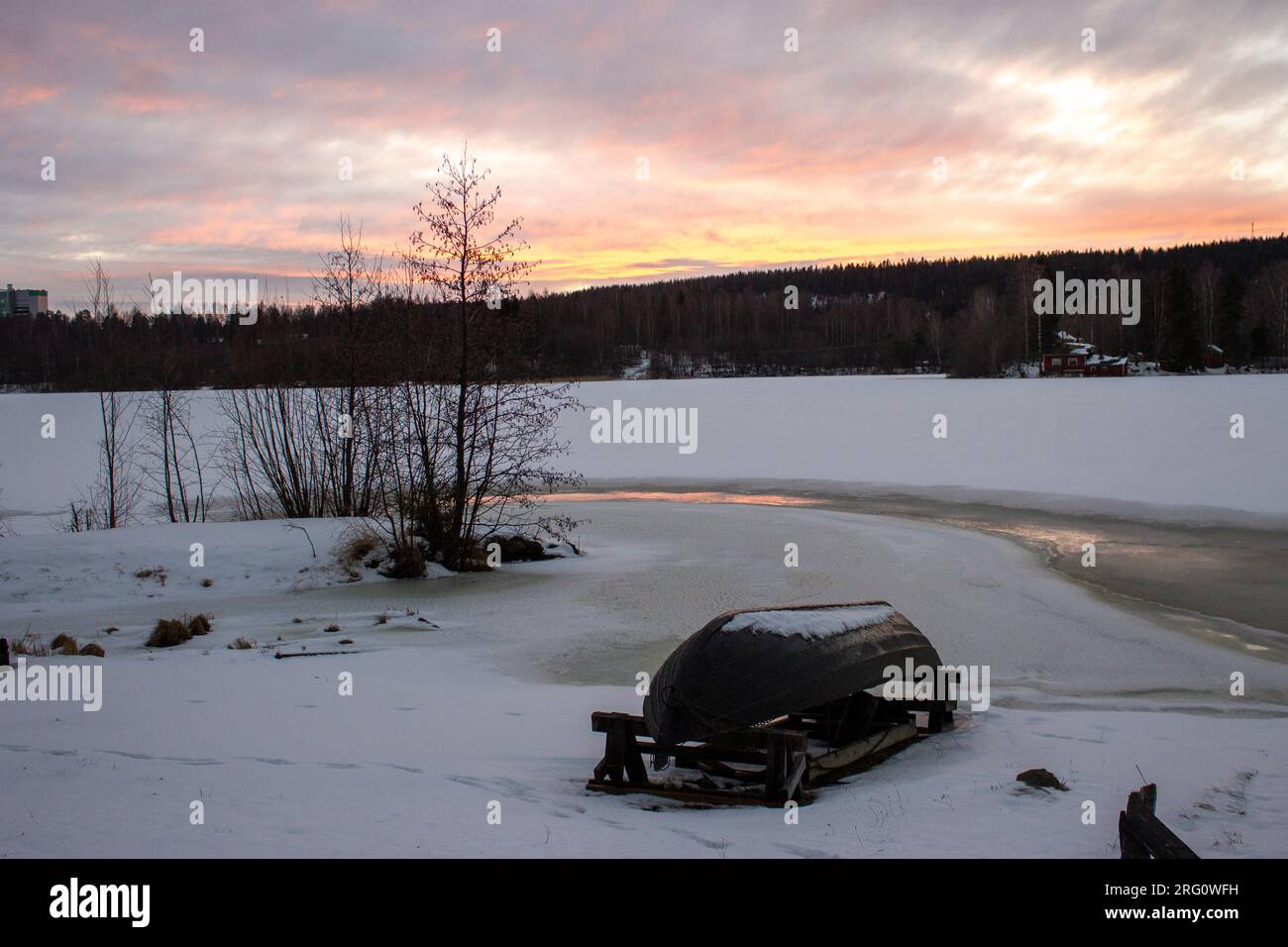 Una tranquilla scena di Kuopio, Finlandia, con una barca capovolta su un lago ghiacciato e un paesaggio al tramonto rosato Foto Stock