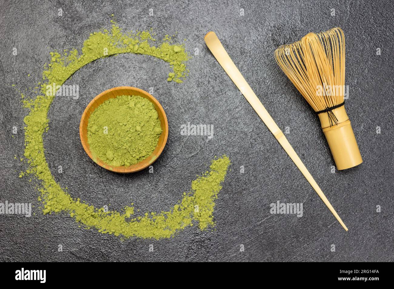 Cucchiaio di bambù e frusta per il tè matcha sul tavolo. Tè Matcha verde in polvere in una ciotola di legno e sul tavolo. Sfondo nero Foto Stock