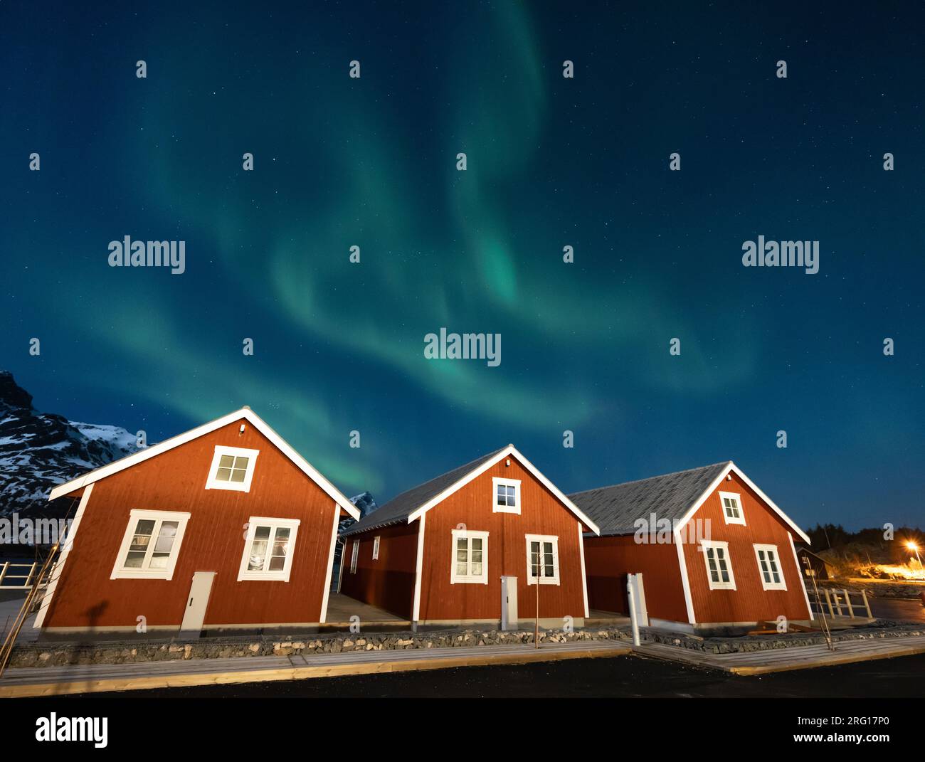 Spettacolare vista delle luci polari verdi nella zona auricolare che si esibiscono in fasce durante la notte contro il cielo limpido sopra il tetto illuminato di legno rosso Foto Stock