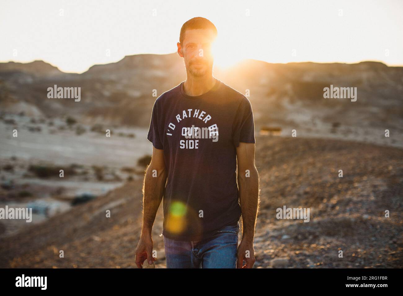 Un giovane uomo in piedi nel deserto che guarda avanti al tramonto Foto Stock