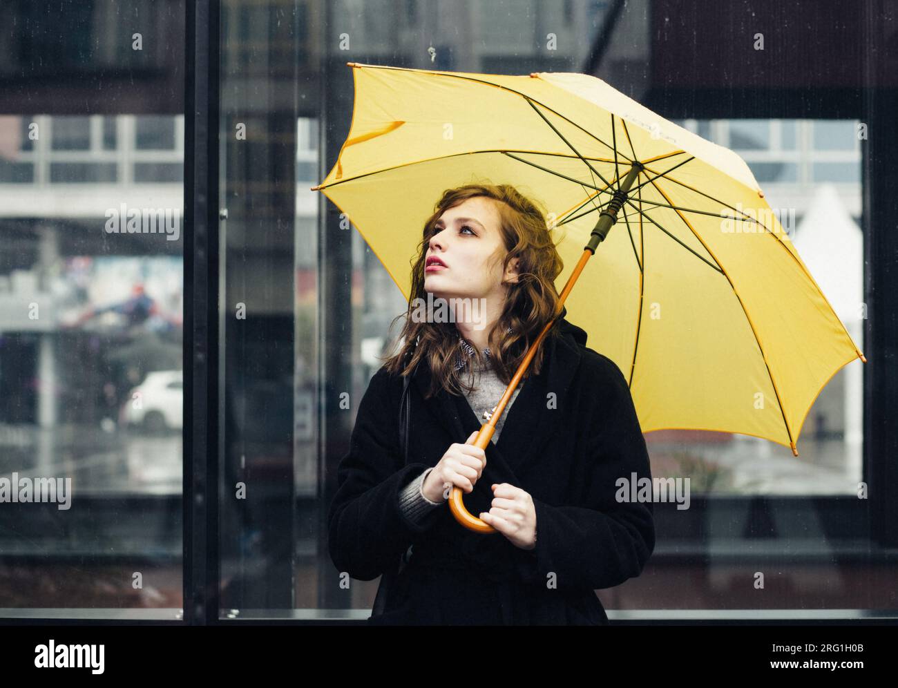 Giovane donna in città con un ombrello giallo Foto Stock