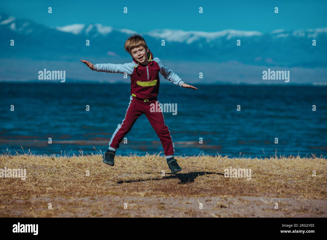 Felice ragazzo che salta sullo sfondo del lago. Issyk-Kul, Kirghizistan Foto Stock