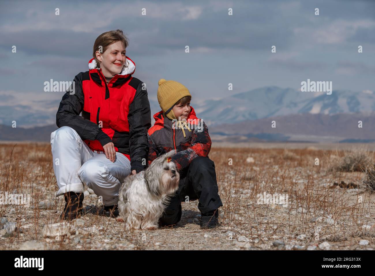 Madre, figlio e cane shih tzu che guarda lontano sullo sfondo delle montagne invernali Foto Stock