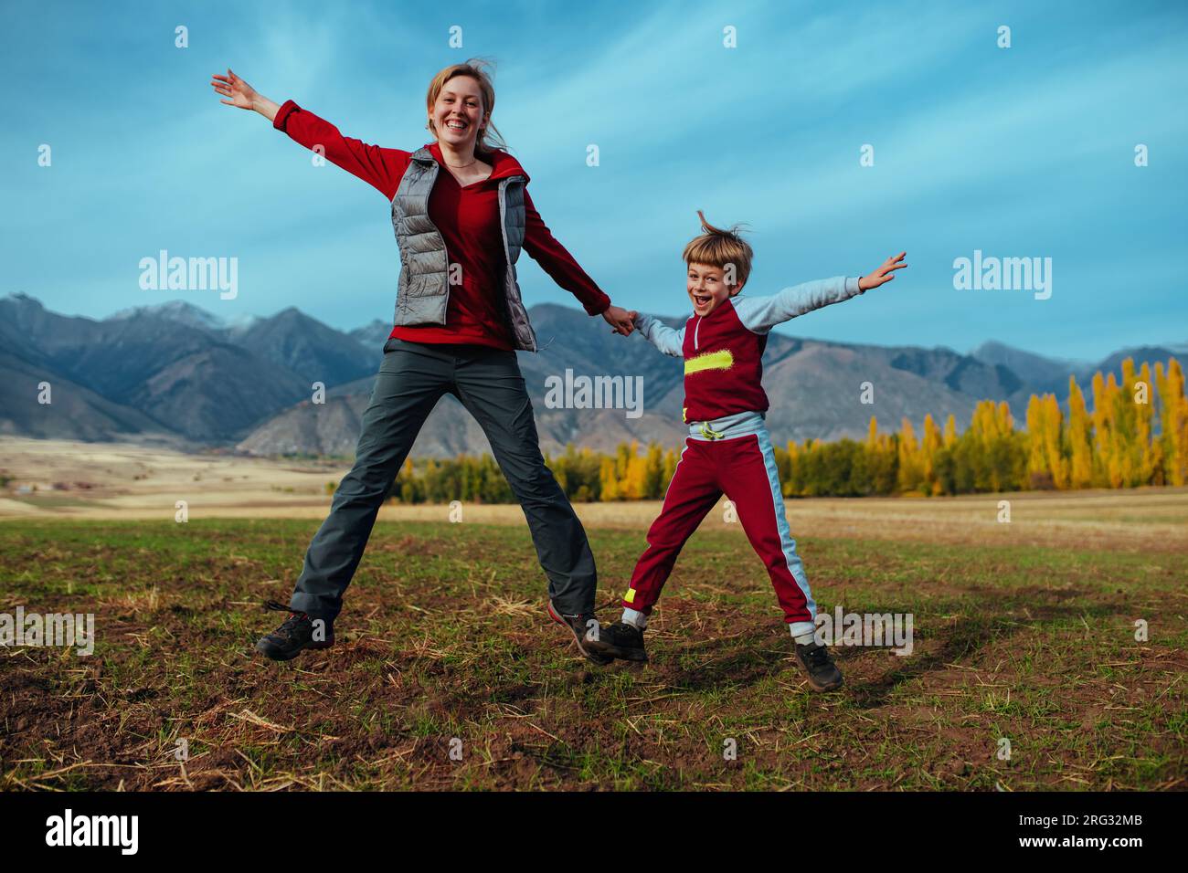 Madre e figlio felici che saltano sullo sfondo delle montagne Foto Stock