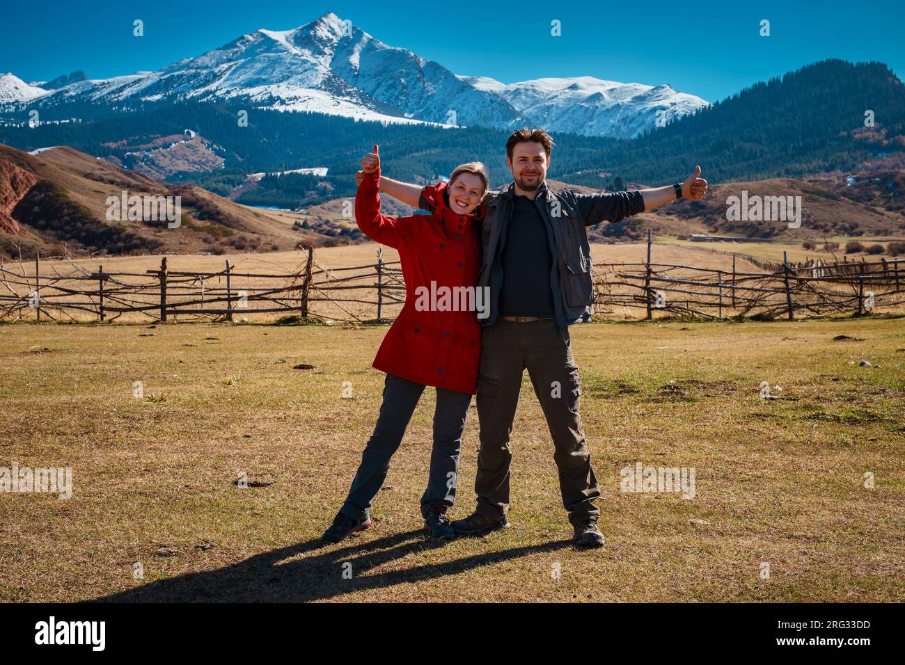 Coppia turistica in posa con i pollici in alto sullo sfondo delle alte montagne Foto Stock