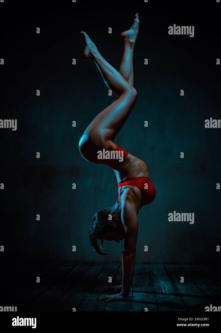Giovane donna sportiva in lingerie rossa in posizione capovolta su sfondo scuro Foto Stock