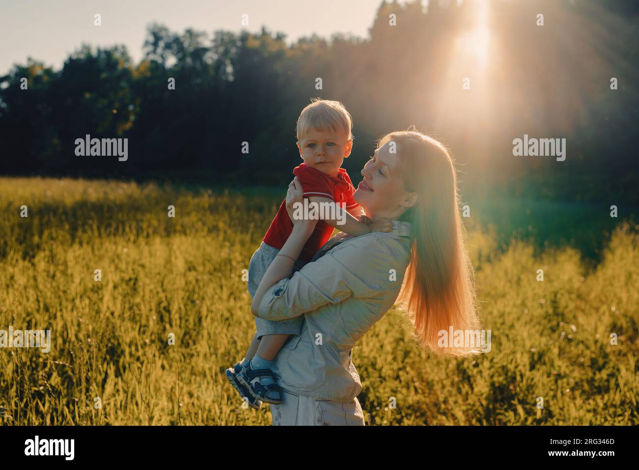Giovane donna felice che tiene un bambino tra le braccia in un campo Foto Stock