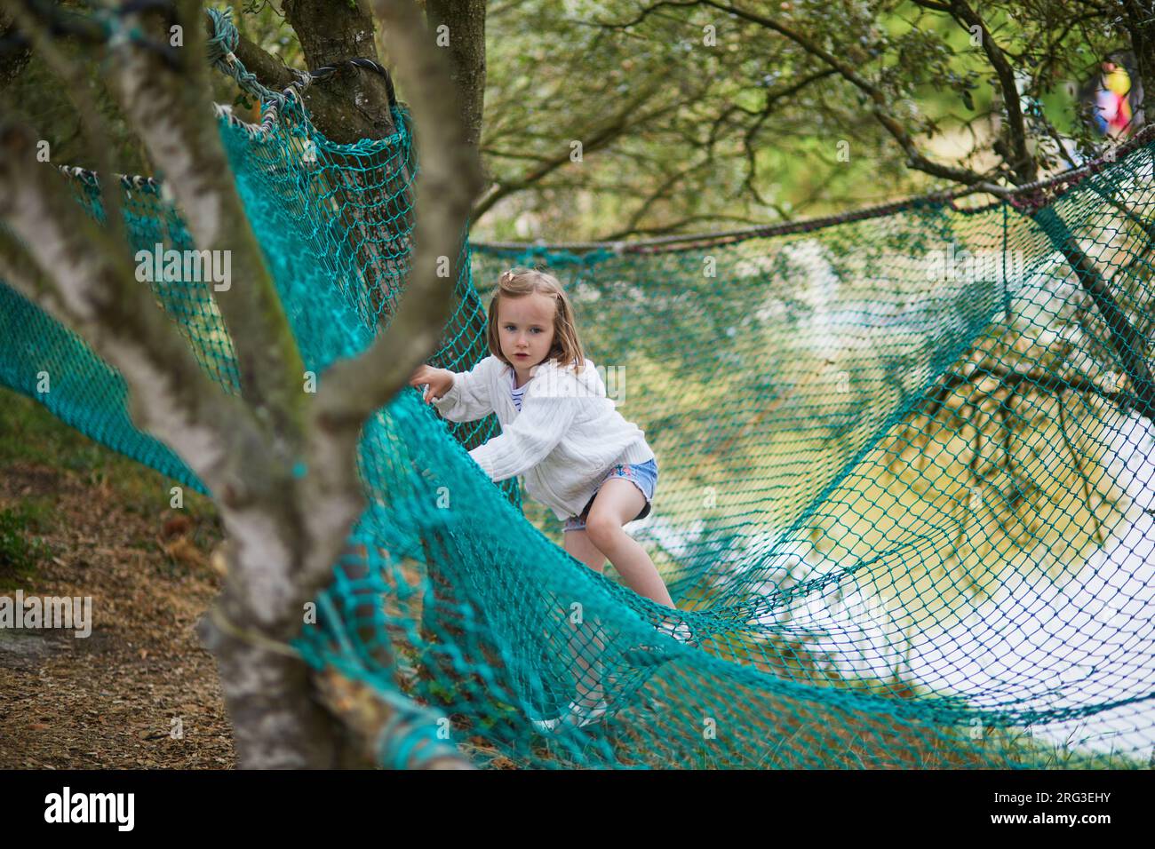 Adorabile bambina in età prescolare che si diverte nel parco avventura. Bambino su trampolino rete superiore. Attività all'aperto per bambini piccoli Foto Stock