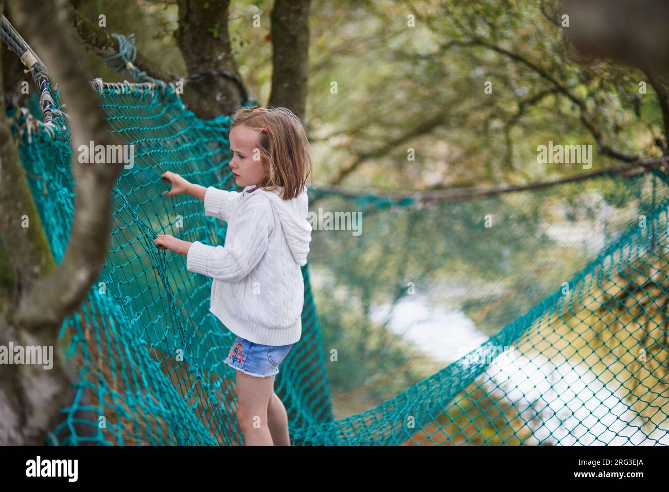 Adorabile bambina in età prescolare che si diverte nel parco avventura. Bambino su trampolino rete superiore. Attività all'aperto per bambini piccoli Foto Stock