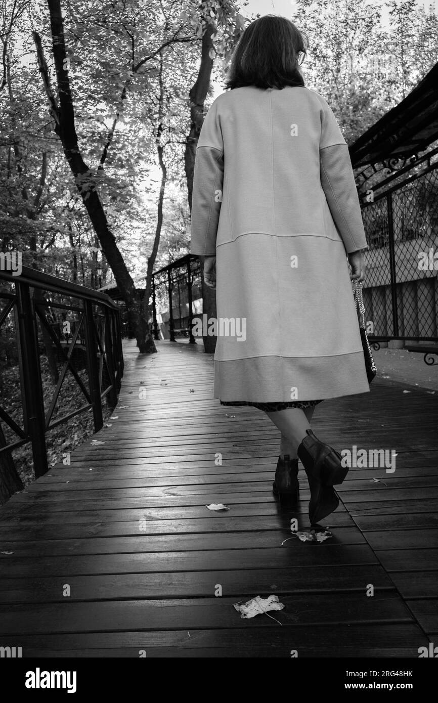 Donna di dietro che cammina da sola, in bianco e nero. Elegante donna solitaria nel parco. Moda autunnale. Stile di vita urbano. La vita in movimento. Foto Stock