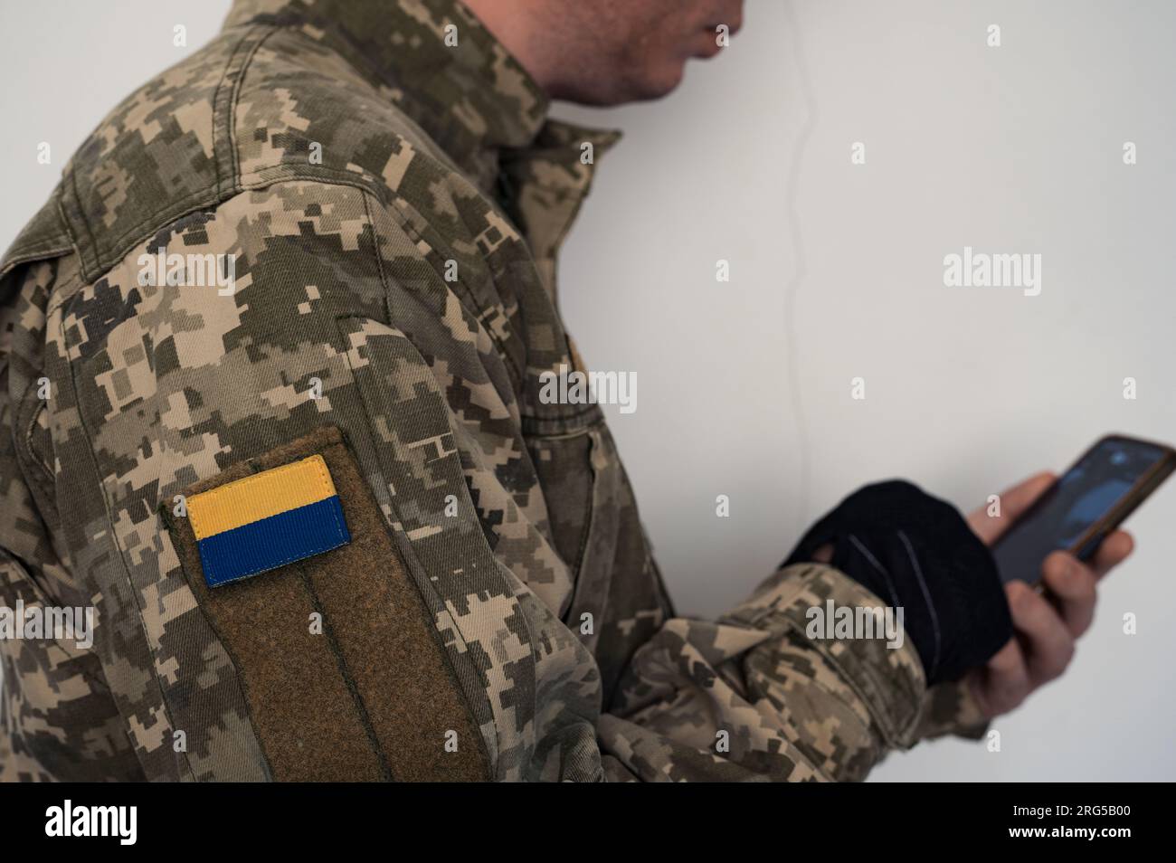 Soldato ucraino in uniforme utilizzando lo smartphone. Uno striscione della bandiera Ucraina su un'uniforme mimetica dei pixel di un soldato. Bandiera Ucraina su chevron Foto Stock