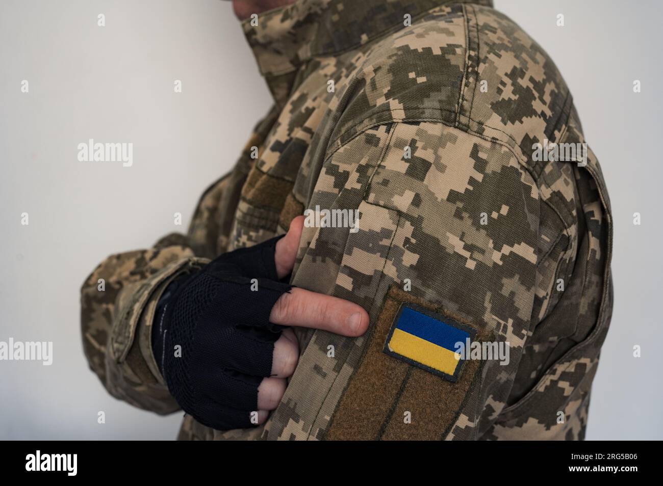 Braccio in guanto di soldato ucraino in uniforme puntare a uno striscione della bandiera Ucraina su una tuta mimetica militare. Pixeled pixel del soldato digitale Foto Stock