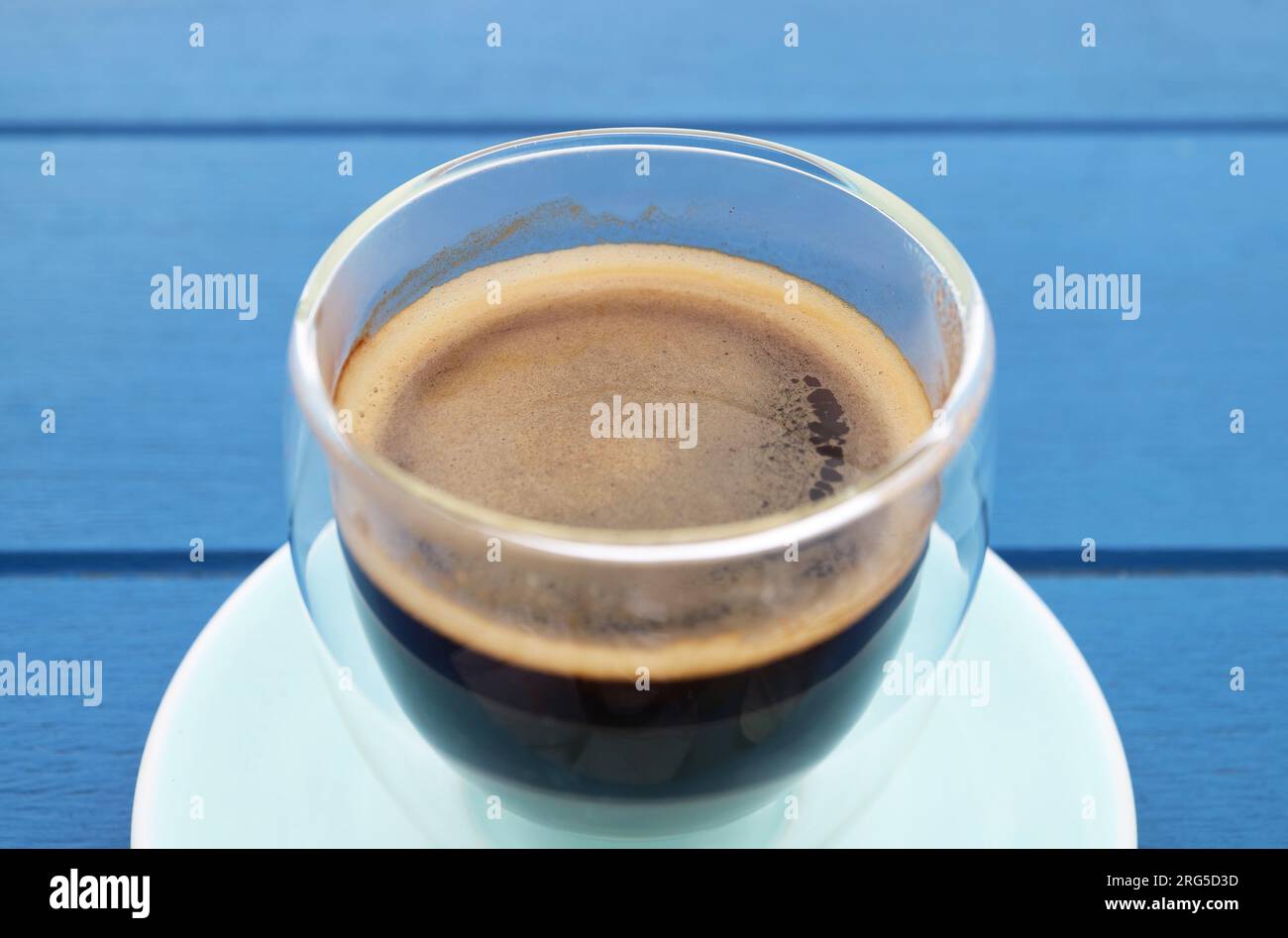 Chiuso un bicchiere di caffè nero caldo isolato su un tavolo di legno blu Foto Stock