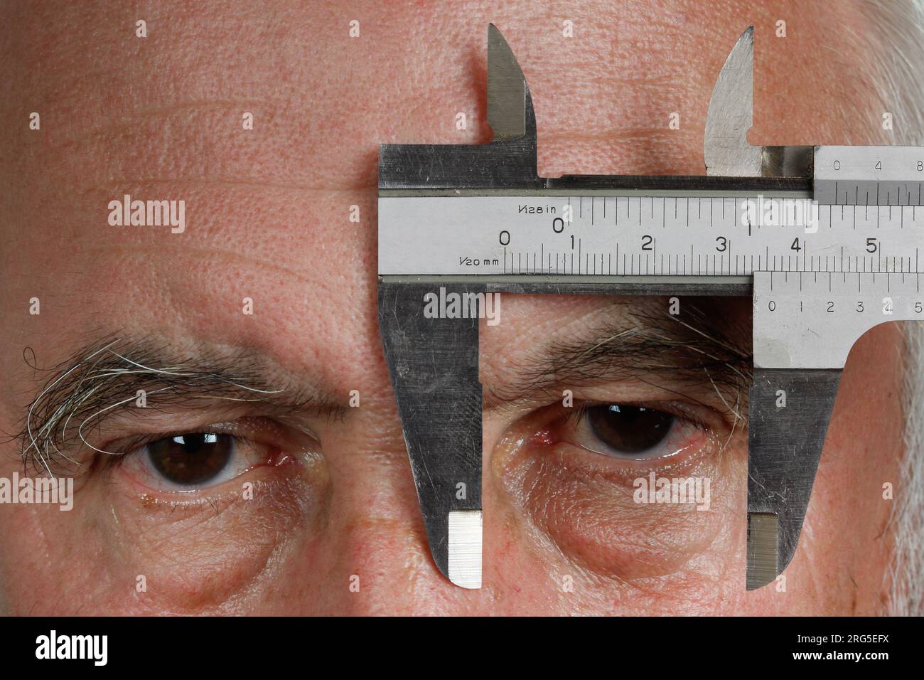 Senso delle proporzioni. Un uomo tiene un calibro davanti all'occhio sinistro e guarda tra le ganasce di misurazione. Foto Stock