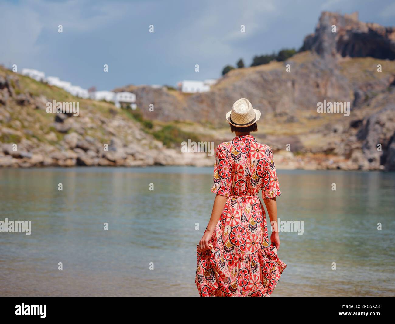 Bella donna felice che si gode le isole greche. Viaggio in Grecia, isole del Mediterraneo fuori stagione turistica. Divertitevi con una vista mozzafiato sul resort sul mare e sulla città vecchia di Lindos sulla montagna Foto Stock